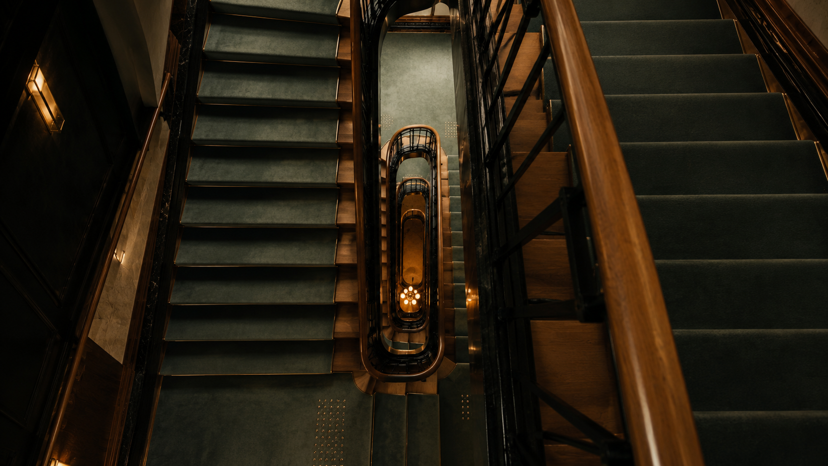 Looking down a dark green and walnut spiral stairwell towards a warmly lit lobby